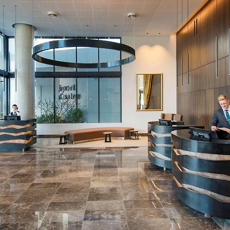 Pullman Brisbane Airport Ξενοδοχείο Εξωτερικό φωτογραφία The image shows a modern hotel lobby. There are two reception desks made of dark-colored materials, and staff members are attending to guests at these desks. The lobby features large windows that allow natural light to fill the space, and there are p